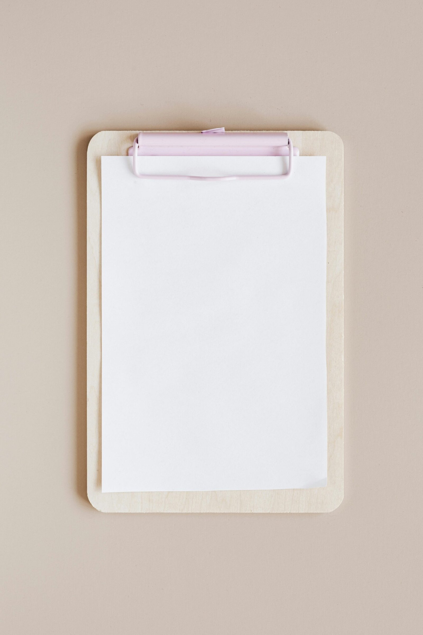 Top view of a minimalist wooden clipboard with blank paper against a neutral background.